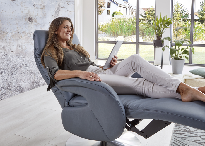 Frau sitzt mit Tablet auf einem Sessel. Fußteil hochgestellt